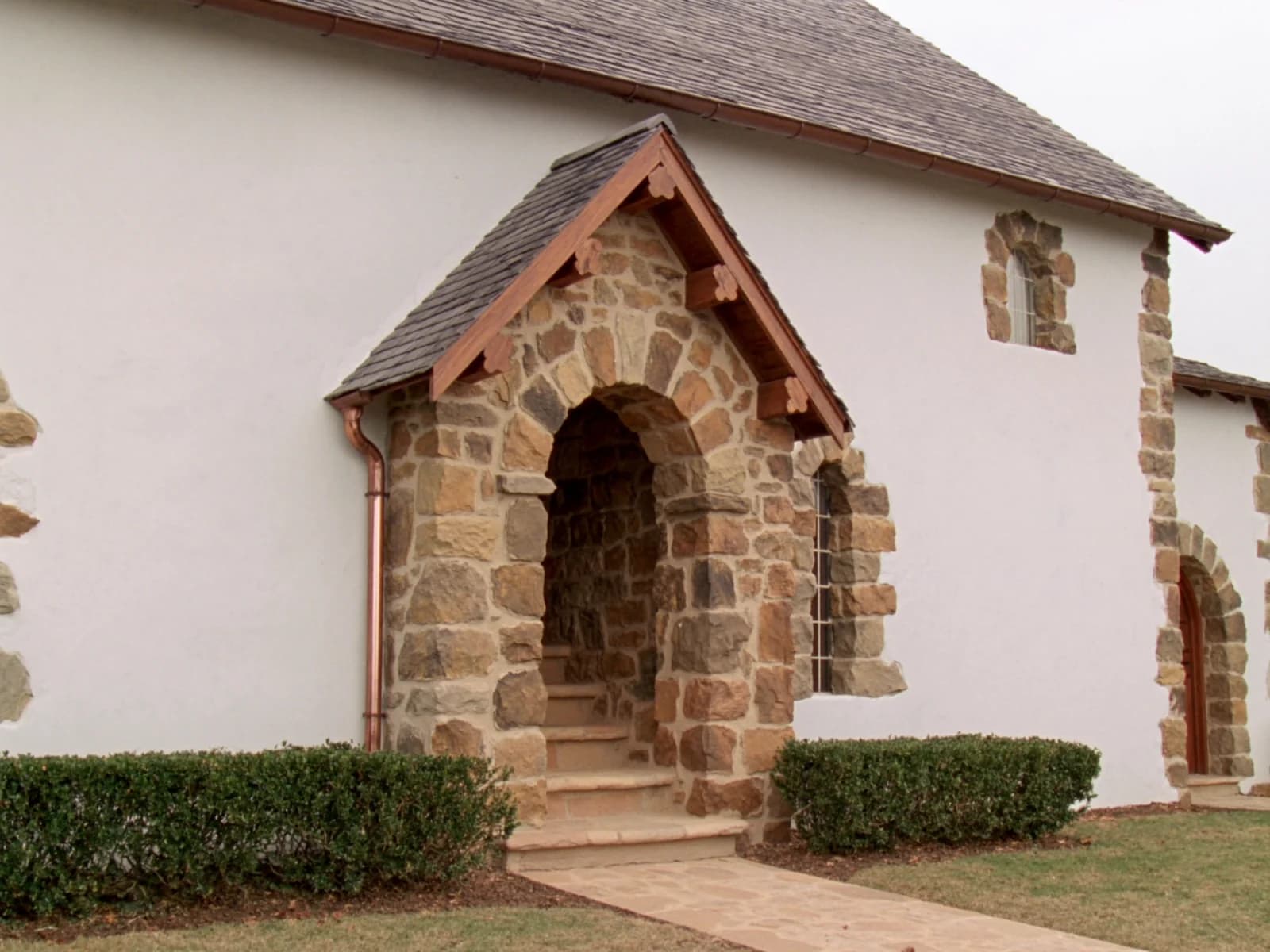 Stone arched entry beneath a steep slate roof, with a copper-trimmed hood