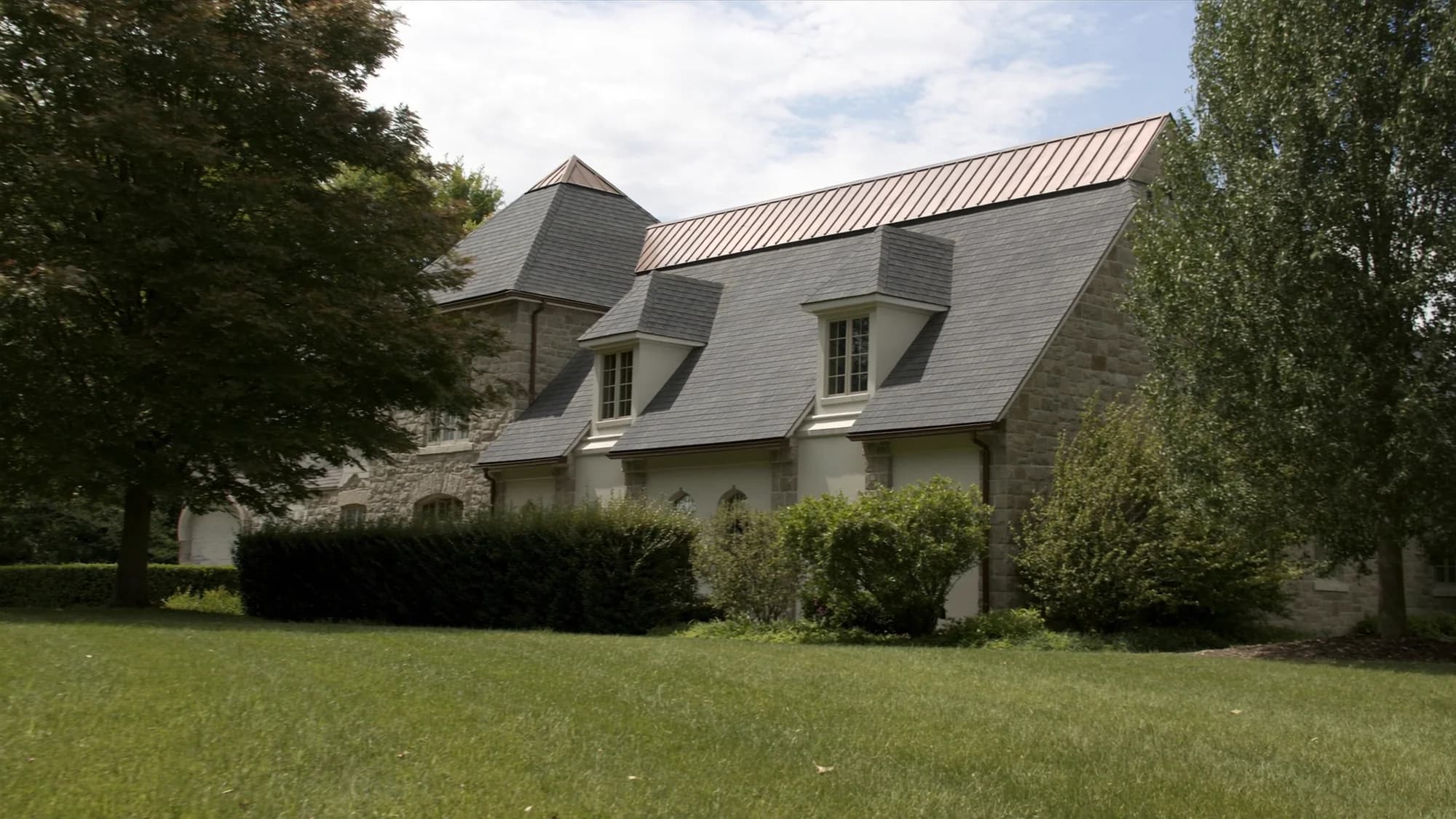 Stone and stucco home with a steep slate roof, dormers and copper valley metal