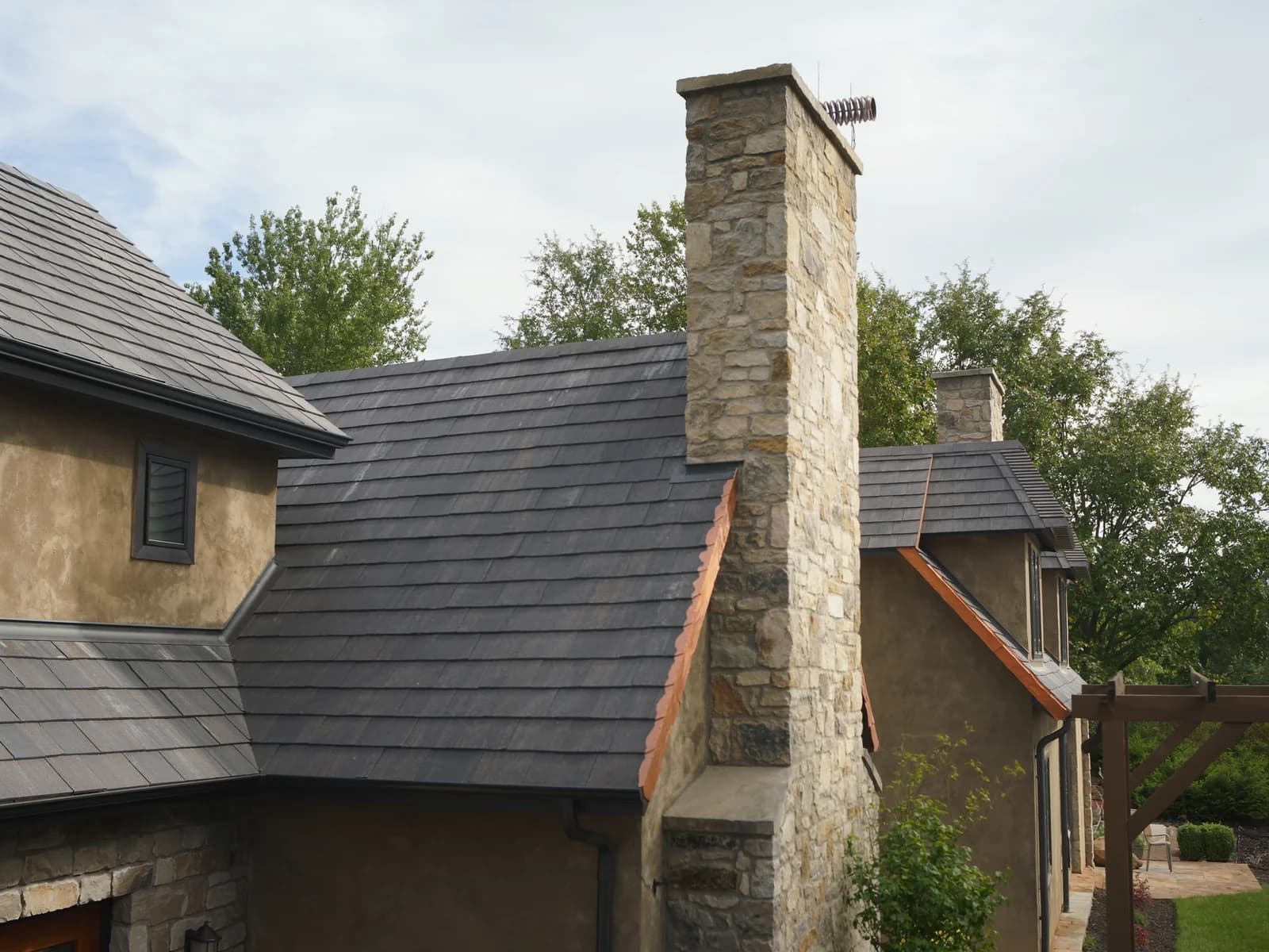 Stone chimney passing through a slate roof, with copper step flashing and a cricket behind it