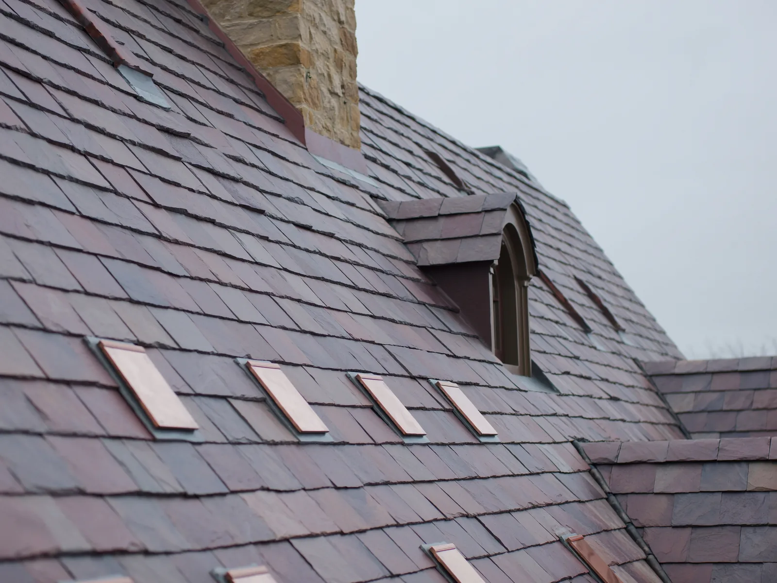Quarried grey-purple slate roof with copper snow guards and a stone chimney
