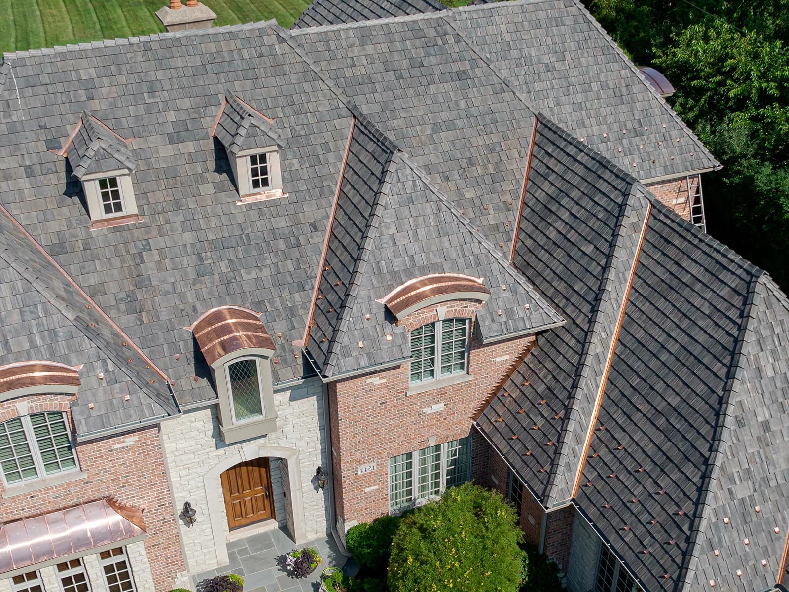 Composite shake roof in a grey blend over a brick home with copper-roofed dormers